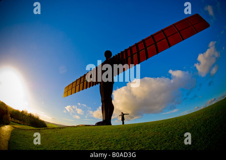 Figura femminile in piedi con braccia tese ai piedi dell'Angelo del Nord a Gateshead. Vista contro un cielo blu. Foto Stock
