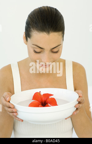 Donna che mantiene hibiscus sbocciare in un recipiente di acqua, guardando verso il basso, sorridente Foto Stock