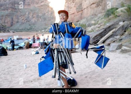 Ragazzo caricato con sedie da campeggio su un banco di sabbia in background il Fiume Colorado nel Grand Canyon Arizona USA MR Foto Stock