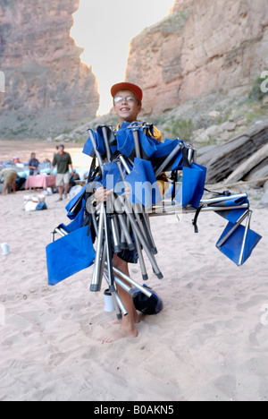 Ragazzo caricato con sedie da campeggio su un banco di sabbia in background il Fiume Colorado nel Grand Canyon Arizona USA MR Foto Stock