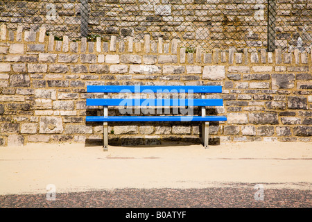 Un vuoto banco blu sul lungomare di Bournemouth. Il Dorset. Regno Unito. Sabbia soffiata fuori dalla spiaggia. Foto Stock