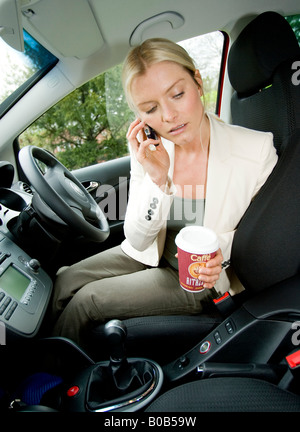 Donna di bere il caffè parlando al telefono in auto Foto Stock
