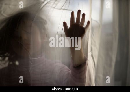 Ragazza di età compresa tra i 4 anni sta dietro tendina Foto Stock