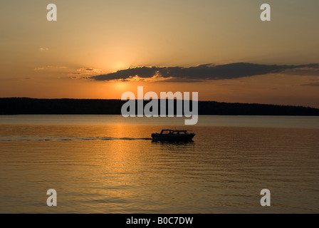 Una barca di uscire al lago contro il sole di setting Foto Stock