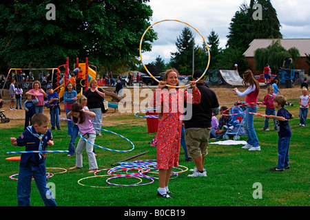 Immagine di una giovane ragazza in piedi trionfante tenendo un hula hoop sopra la sua testa come un gruppo di altri bambini continuano a ballare Foto Stock