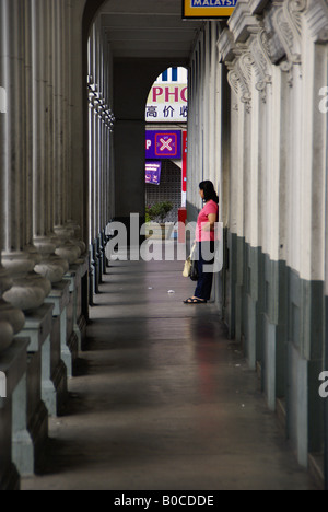 Una donna in attesa di un autobus al di fuori del centro di Kuching Post Office Foto Stock