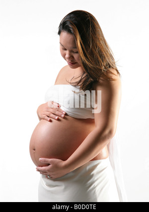 Giovani incinta donna asiatica da soli cullano grembo Foto Stock