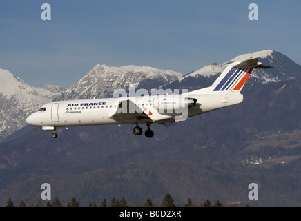 Commerciale viaggi dell'aria. Air France Fokker 70 jet atterraggio aereo con le montagne sullo sfondo, che simboleggiano l'impatto dei trasporti aerei sull'ambiente. Foto Stock