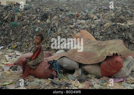 Little Boy tenere un occhio sul rubbsih durante l'attesa per la sua mamma per andare a casa dopo il lavoro di finitura a dumpsite in phnompenh. Foto Stock