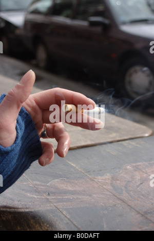 Sigaretta accesa in mano su una strada di città Foto Stock