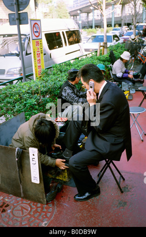 Novembre 17, 2004 - Uomo in un vestito con il suo telefono cellulare mentre avente le sue scarpe risplendeva al di fuori della stazione di Tokyo nel centro di Tokyo. Foto Stock