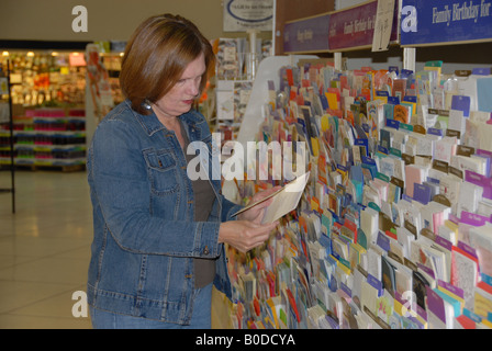 Una donna guarda attraverso i biglietti di auguri presso un negozio di alimentari. Foto Stock