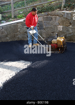 Giorno operaio stamping giù su asfalto appena costruito passo carraio Foto Stock