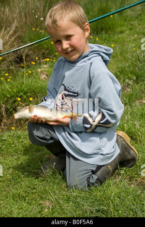 Stock Foto di un bambino di otto anni con orgoglio la visualizzazione di una carpa ha appena pescato nel lago Foto Stock