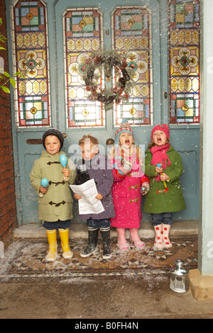 Quattro bambini cantare i canti natalizi nella neve sul gradino della porta di una bella casa Foto Stock