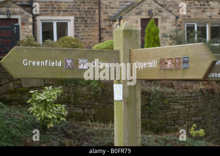 Segno che mostra il modo di Greenfield e Uppermill in Saddleworth, nello Yorkshire, davanti al cottage in pietra tipico della regione Foto Stock