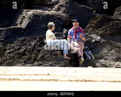 Vecchia coppia sat sulle rocce in spiaggia, parlando. Foto Stock