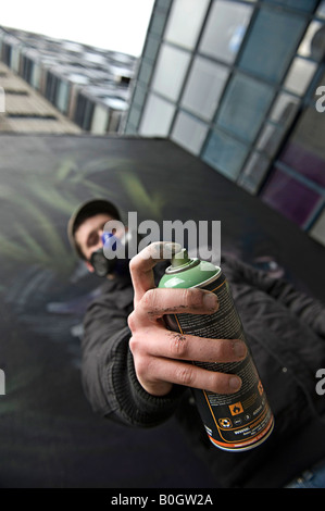 Artista di graffiti con maschera di vernici a spruzzo di un murale su una parete Foto Stock