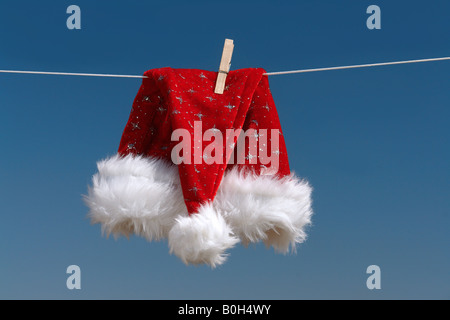 Rosso di santa claus hat asciugatura all'aria aperta appeso sulla linea di abbigliamento apposta con spina in legno Foto Stock