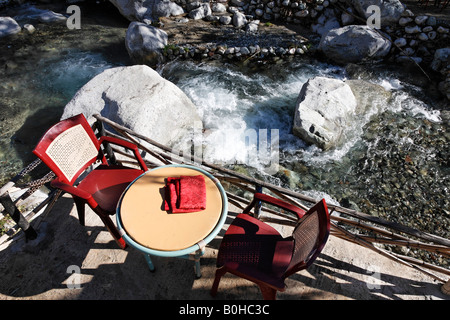 Due sedie rosse e un tavolo in un ristorante patio con vista sul monte rapids, Ourika Valley, Alta gamma Atlas, Marocco, a nord di un Foto Stock