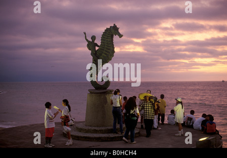 Turisti che si godono la vista al tramonto al di sotto di una statua di una persona che guida un cavalluccio sulla promenade della spiaggia di Puerto Vallarta, Jal Foto Stock
