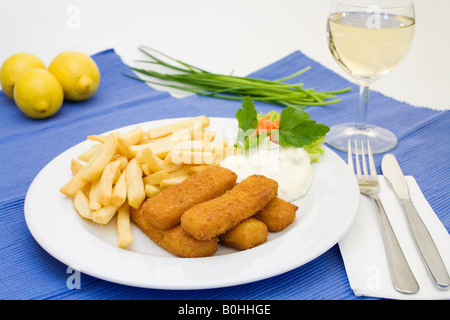 Bastoncini di pesce, salsa tartara e patatine fritte servite con un bicchiere di vino bianco, limoni e erba cipollina Foto Stock