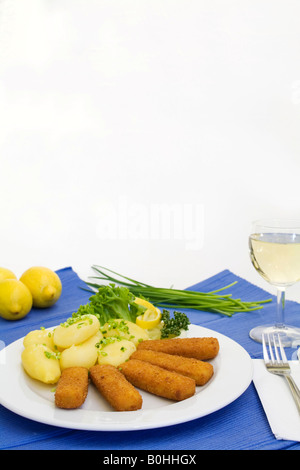 Bastoncini di pesce, salsa tartara e patatine fritte servite con un bicchiere di vino bianco, limoni e erba cipollina Foto Stock