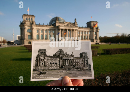 Di allora e di oggi, la mano che tiene una vecchia foto in bianco e nero del Reichstag tedesco o Case del Parlamento mostra la seconda guerra mondiale bomba d Foto Stock