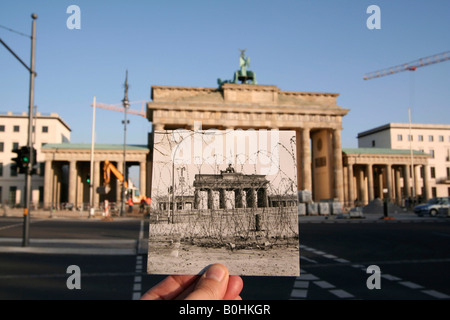 Di allora e di oggi, la mano che tiene una vecchia foto in bianco e nero di Brandenburger Tor o Porta di Brandeburgo che mostra il muro di Berlino e ba Foto Stock