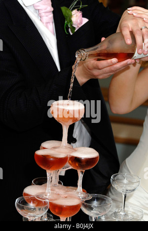 La sposa e lo sposo versando rosa vino spumante in una cascata di champagne al loro ricevimento di nozze. Questo celebra il loro matrimonio Foto Stock