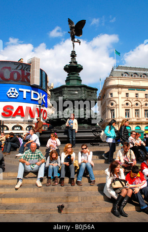 Piccadilly Circus statua di Eros eretta nel 1892 con i turisti seduti sui gradini e vistose annunci pubblicitari in background in primavera Foto Stock