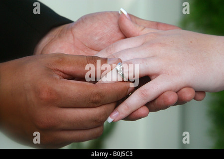 Dark scuoiati groom posizionando l'anello nuziale sulla sposa caucasica Foto Stock