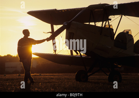 Pilot vicino ad un vecchio biplano trainer De Havilland DH 82c Tiger Moth sul tramonto Foto Stock