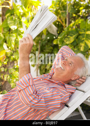 Uomo disteso su una lounge chair leggendo il giornale, vista laterale Foto Stock