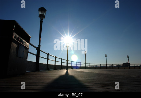 I lampioni si stagliano contro il cielo blu senza nuvole accanto a una lettiera bin su Worthing Pier, Inghilterra. Foto Stock