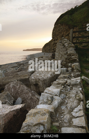 Parete costa cliff bay ciottoli crepuscolo alba sunrise tramonto arancione bagliore orizzonte acqua di mare robusto umore Moody desolazione di salita Foto Stock