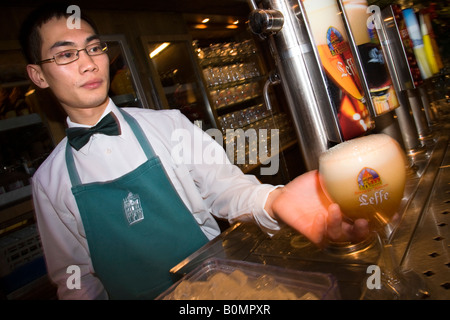 Barman cinese serve un belga Leffe birra in Le Roy d'Espagne bar. La Grand Place di Bruxelles. Belgio Foto Stock