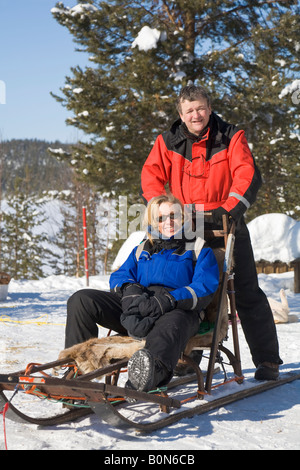 Una donna e un uomo su una slitta durante una corsa in viaggio con i cani da slitta in Lapponia winterly / Svezia settentrionale Foto Stock