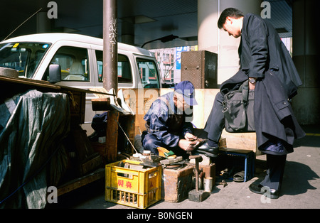 Uomo in una tuta avente le sue scarpe irraggiata da un uomo anziano al di fuori della stazione di Shibuya di Tokyo centrale. Foto Stock