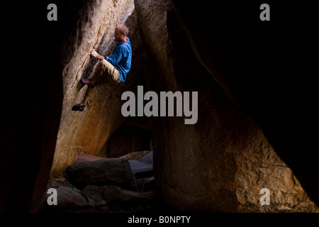 Maschio di rocciatore bouldering in una grotta-come zona di Hampi India Foto Stock