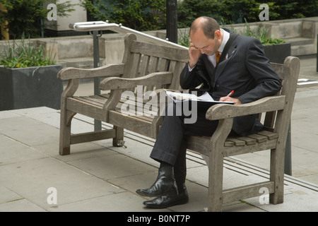 Mancino city professional imprenditore telefona sul suo telefono cellulare mentre seduto su un pubblico di Londra banco. Foto Stock