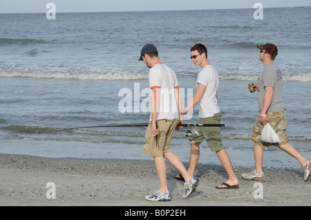 Tre giovani uomini a piedi lungo la spiaggia di caccia Island in South Carolina, Stati Uniti d'America. Sono in corso attività di pesca. Foto Stock