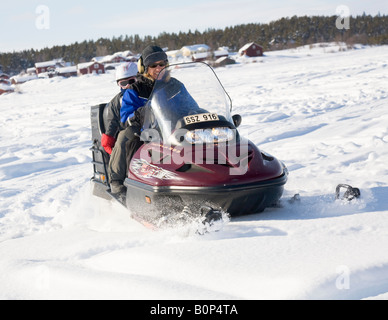 Una donna nel suo fourties cavalca un Lynx snowmobile in Lapponia nevoso, a sei anni ragazza è seduta sul sedile posteriore Foto Stock