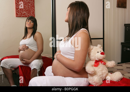 36 settimana di gravidanza teenage donna con pancia esposta a sedersi guardando a se stessa nella sua camera da letto specchio Foto Stock