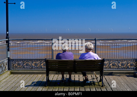 La spiaggia a Skegness in Lincolnshire Inghilterra con una offshore wind farm visibile all'orizzonte e due vecchie signore guardando fuori Foto Stock