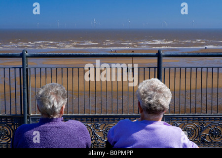 La spiaggia a Skegness in Lincolnshire Inghilterra con una offshore wind farm visibile all'orizzonte e due vecchie signore guardando fuori Foto Stock