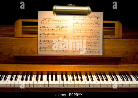 A 40 anno vecchio legno di ciliegio pianoforte con foglio di musica illuminata da una piccola lampada da lettura Foto Stock