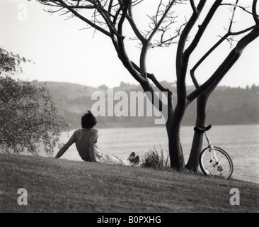 Immagine in bianco e nero di un uomo e di monociclo riposo sotto un albero Foto Stock