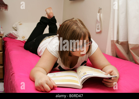 Studentessa giacente sul letto dalla lettura di un libro di testo Foto Stock