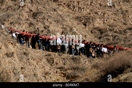 Una lunga fila di monaci carrieng è un enorme Tanka fino a maountain nel monastero di Labrang nella Provincia di Qinghai Cina Foto Stock